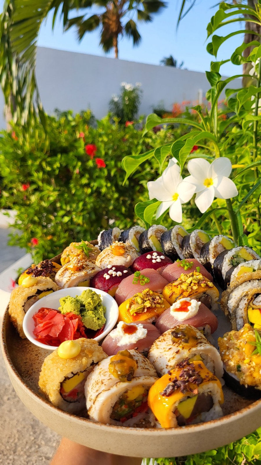 Un generoso plateau di sushi KAMI sollevato davanti alle palme e ai fiori di frangipane di Zanzibar