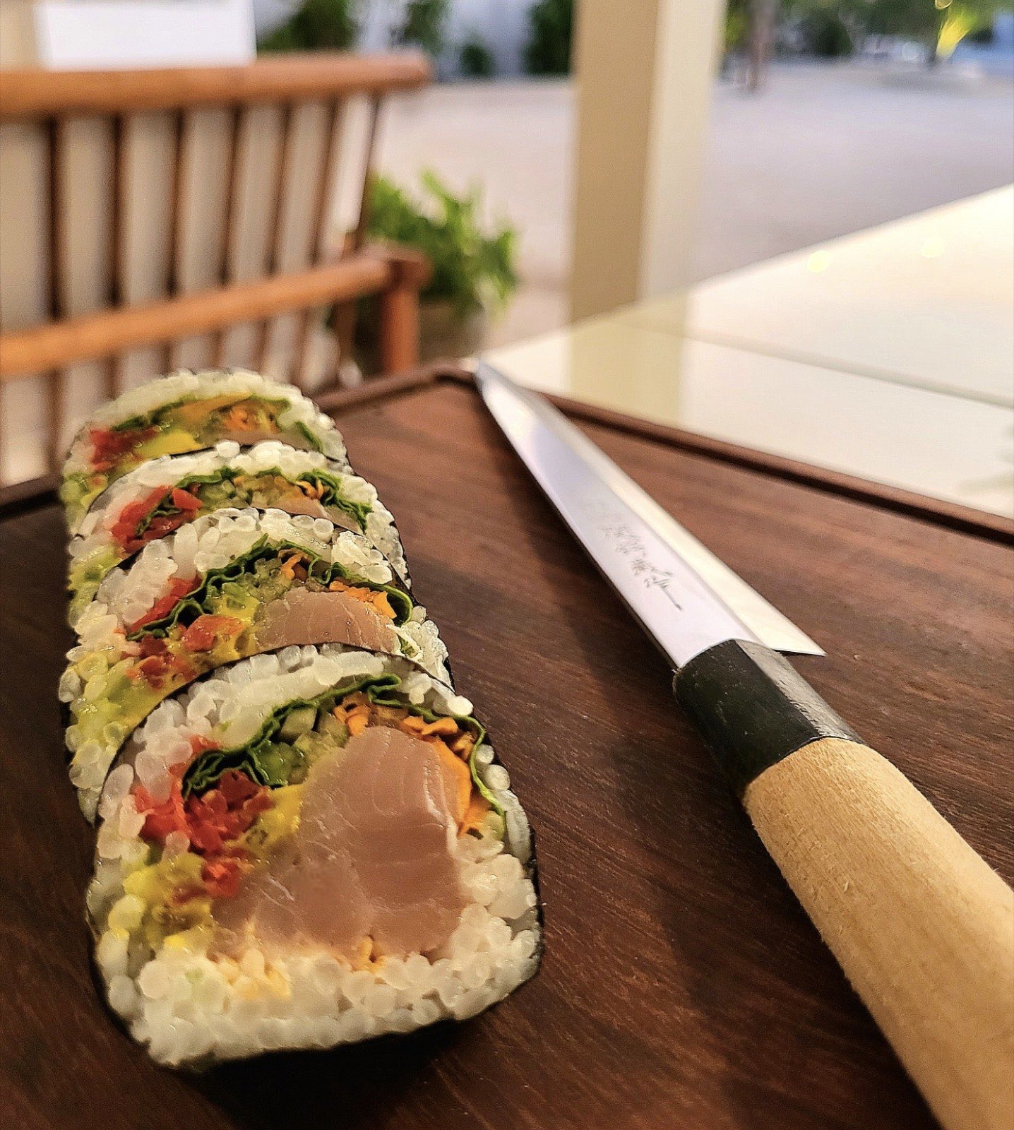 Un futomaki tagliato a fette accanto a un tradizionale coltello da sushi yanagiba