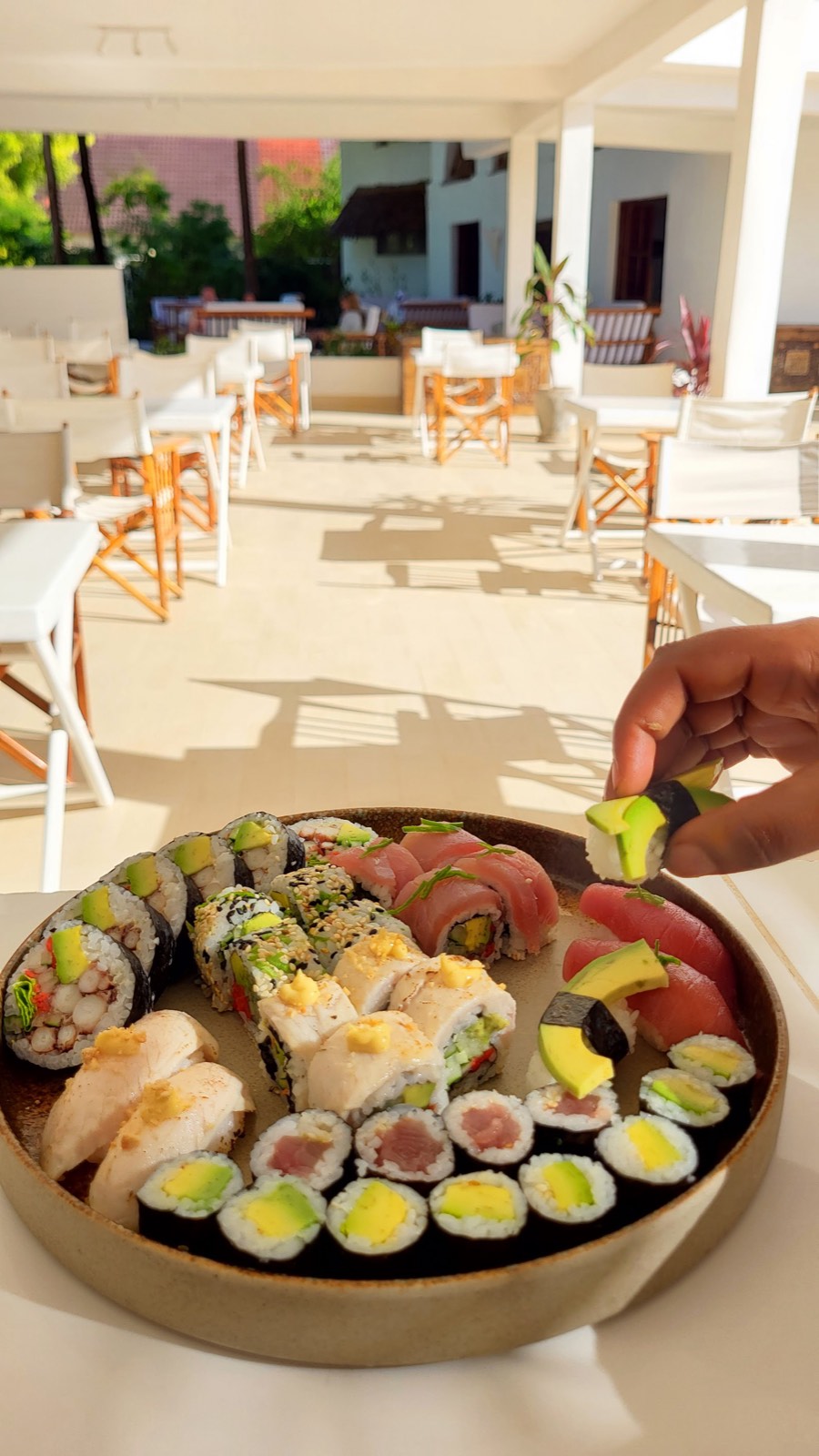 Una mano che prende un pezzo di sushi da un plateau sulla terrazza soleggiata di KAMI