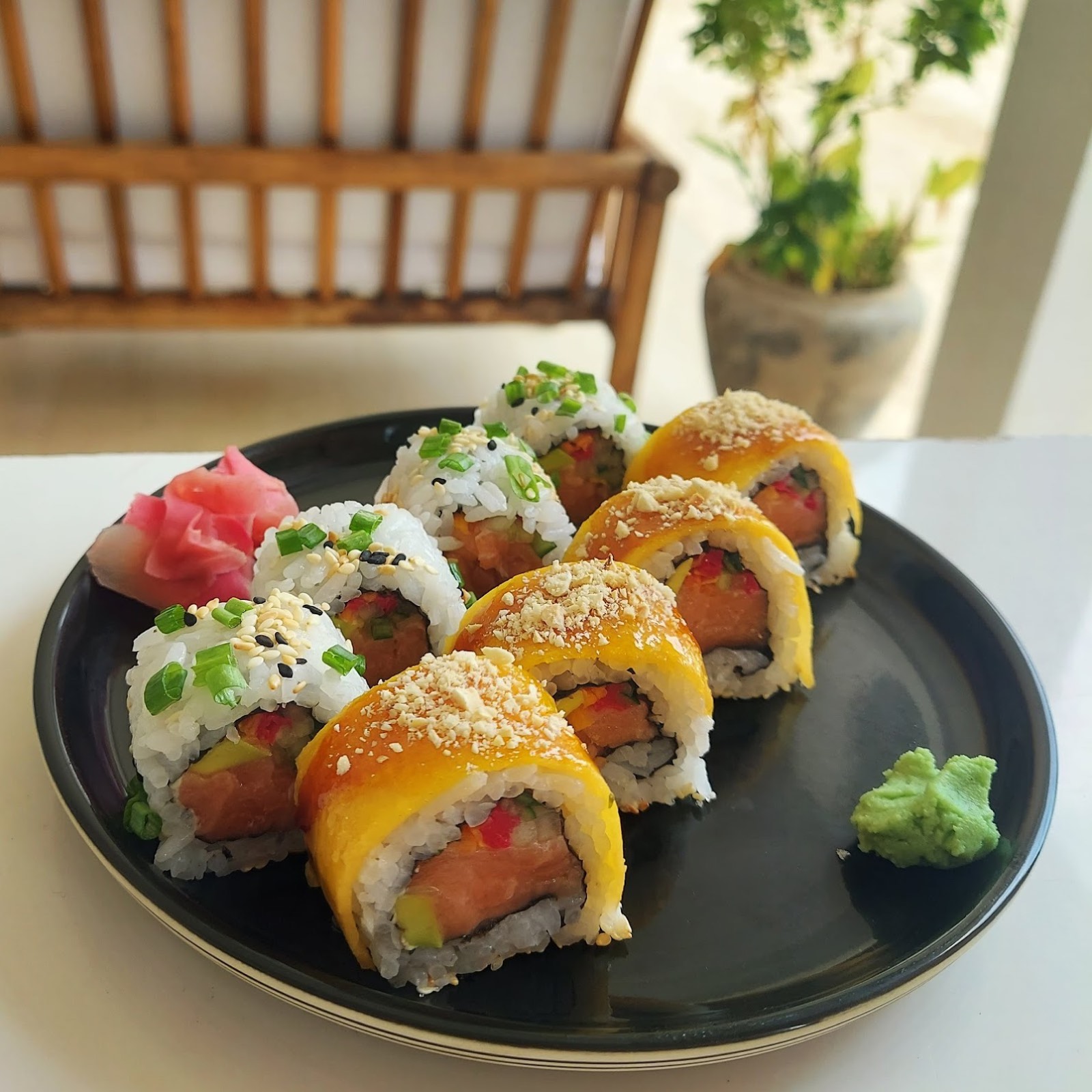 Roll di salmone ricoperti di mango con zenzero marinato e wasabi su un piatto nero